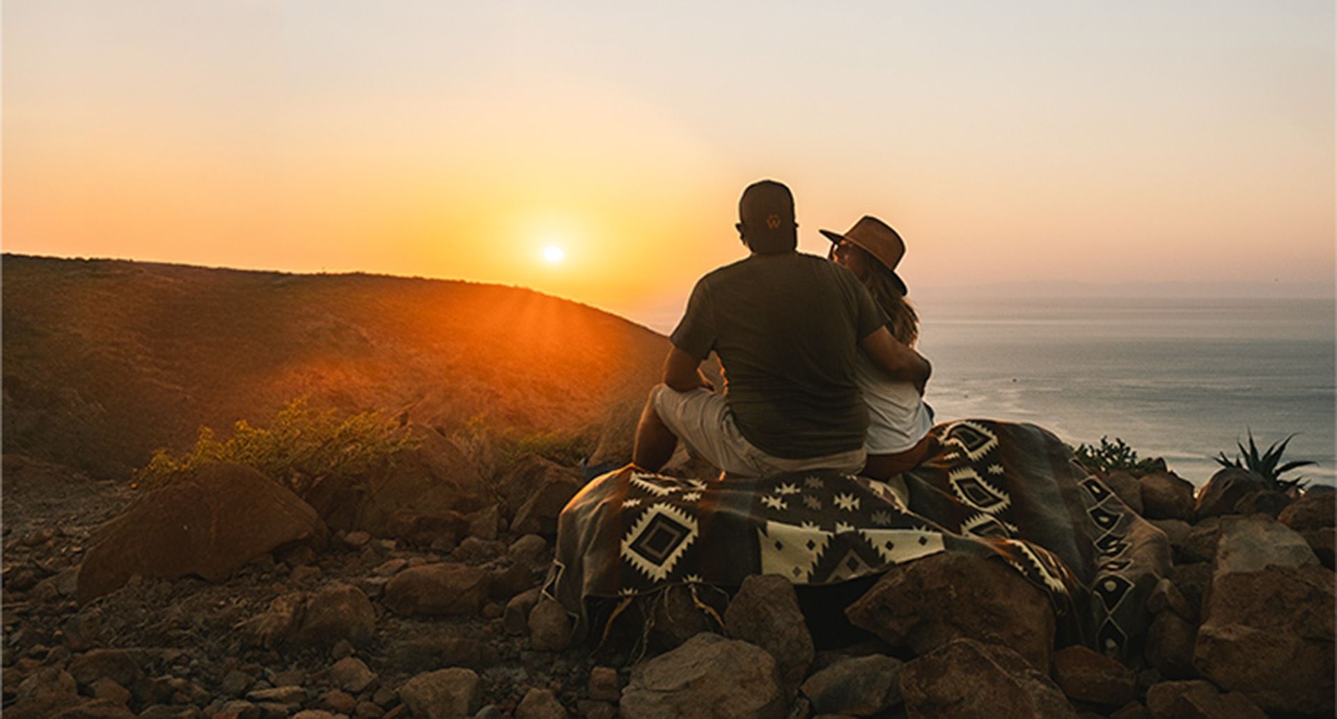 couple sitting on a hilltop looking at the sunset over the next hilltop
